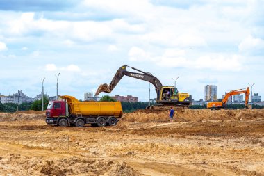 MINSK, BELARUS - 2 Temmuz 2021: Açık sarı ağır sanayi kazıcısı kentteki inşaat sahasında çalışıyor.