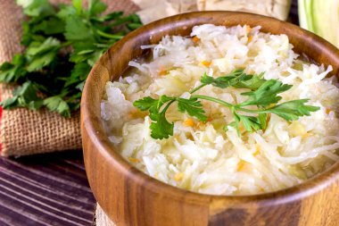 Lezzetli lahana turşulu kahverengi yuvarlak ahşap kase ve kırsal zeminde maydanozlu havuç..