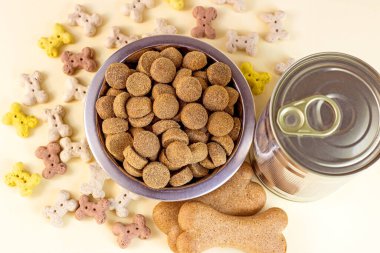 Kahverengi bisküvi kemiklerinin üst görüntüsü, hafif arka planda beslenmek için gevrek organik mama parçaları ve metal kutuda ıslak köpek maması..