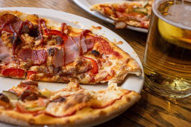 Peynirli ve etli bir dilim taze pizza yemek ve restoranda bir bira içmek..