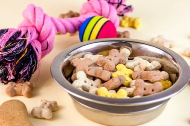 Kahverengi bisküvi kemikleri ve hafif arka planda farklı oyuncakları olan köpek maması için gevrek organik mama parçaları. Sağlıklı kuru hayvan maması konsepti.