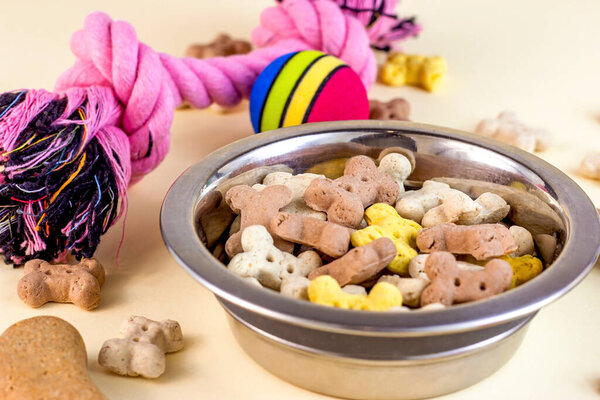 Кости коричневого печенья и хрустящие органические кусочки корма для собак с различными игрушками на светлом фоне. Здоровый сухой корм для домашних животных.
