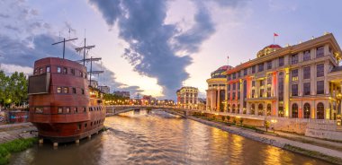 Üsküp şehir merkezinde gün batımında şehir ışıkları Vardar Nehri 'ni yansıtıyor. Kuzey Makedonya.