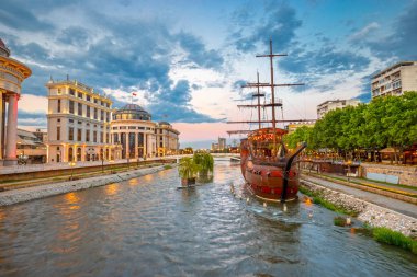 Günbatımında Üsküp, Kuzey Makedonya 'nın merkezi, Vardar nehri, gemi ve çevresindeki binalarla geniş bir manzara.