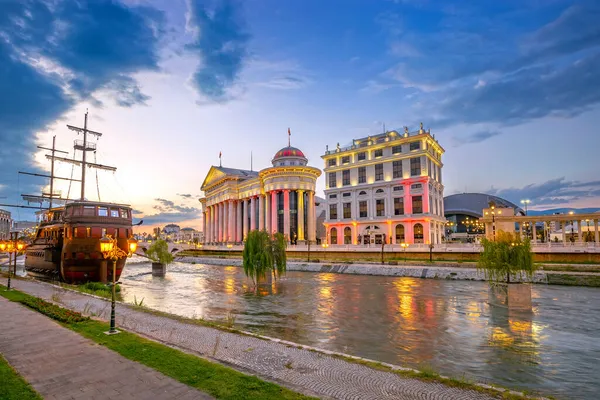 Vardar川の光の反射を持つSkopjeの美しい夕日 マケドニア考古学博物館と日没の文明の橋 川の古い船 — ストック写真