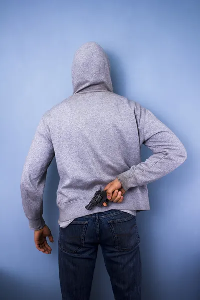 З капюшоном чоловік ховає пістолет за спиною — стокове фото
