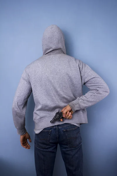 Homem encapuzado escondendo arma nas costas — Fotografia de Stock