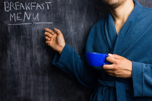 Hombre en bata señalando el menú del desayuno en la pizarra —  Fotos de Stock