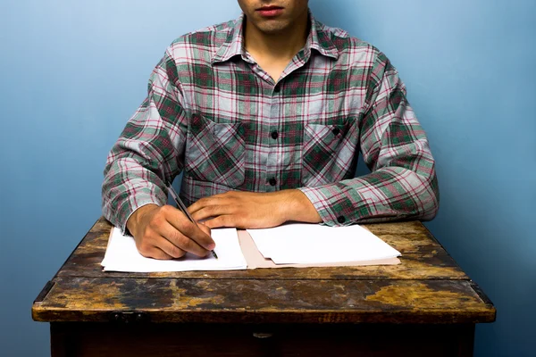 Молодой человек пишет за столом — стоковое фото
