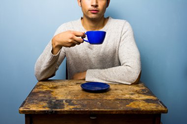 genç adam, ahşap masadaki bardaktan içiyor