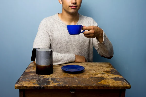 Mladý muž u dřevěného stolu, pije cofffee — Stock fotografie