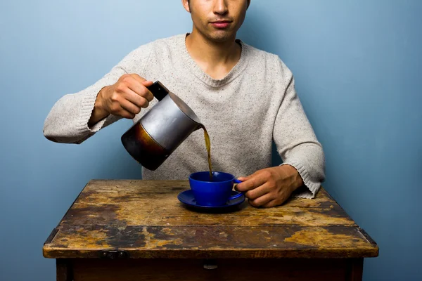 Jeune homme à la table en bois versant café — Photo