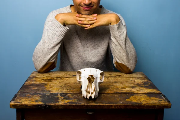 Улыбающийся человек с черепом за столом — стоковое фото