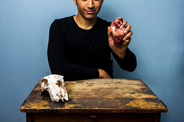 Молодий чоловік тримає серце тварини біля козячого черепа — стокове фото