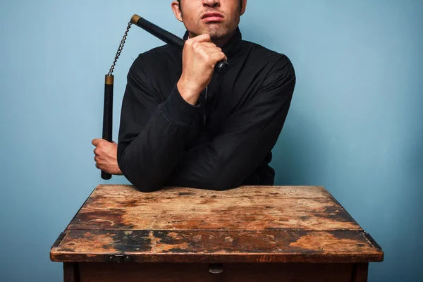 Thug at table with nunchucks — Stock Photo, Image