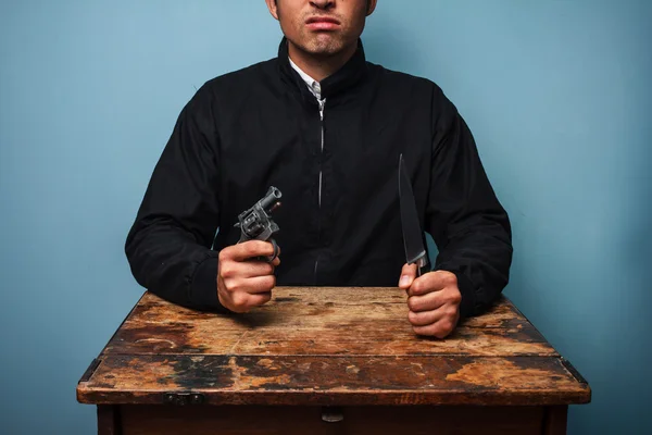 Thug aan tafel met pistool en mes — Stockfoto