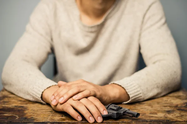 Man at table with a gun — Stock Photo, Image