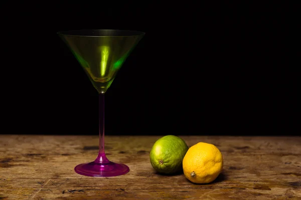 Copo de cocktail e limão e limão na superfície de madeira — Fotografia de Stock
