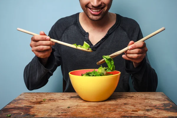 Glücklicher Mann mixt Salat mit Holzlöffeln — Stockfoto