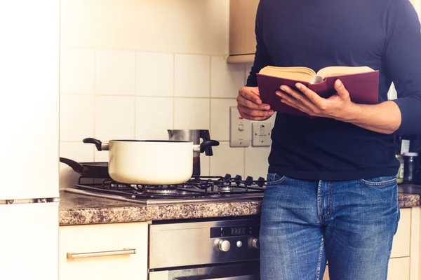 Uomo che legge grande libro di cucina in cucina — Foto Stock