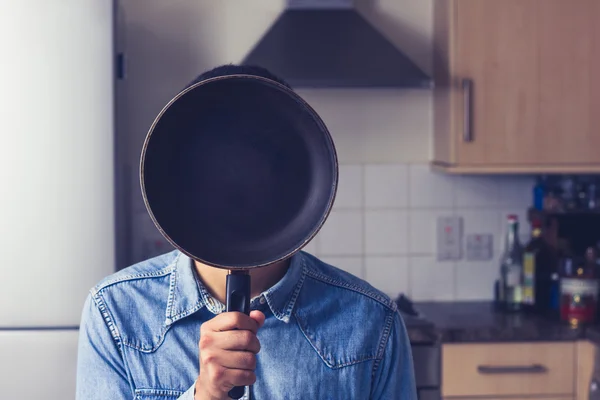 Mutfakta tavada yüzünün önünde tutan adam — Stok fotoğraf