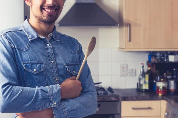 Jovem feliz com colher de madeira na cozinha — Fotografia de Stock