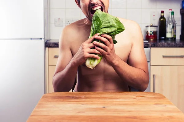 Homem nu na cozinha comer alface — Fotografia de Stock