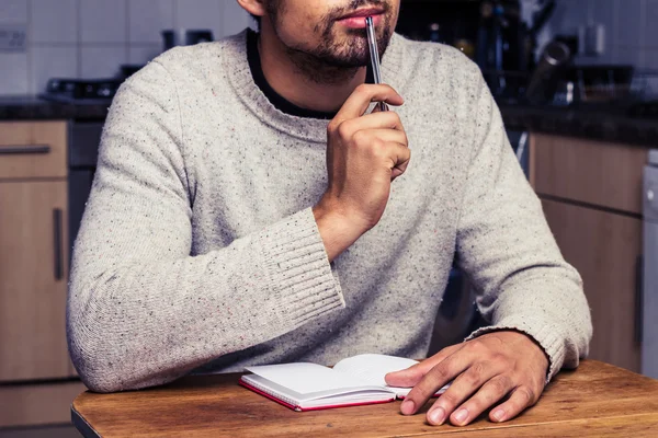 Man in kitchen is thinking and writing — Stock Photo, Image