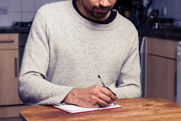 Young man writing in kitchen — Stock Photo, Image