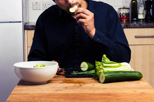 Man making a salad and eating cucumber — Stock Photo, Image