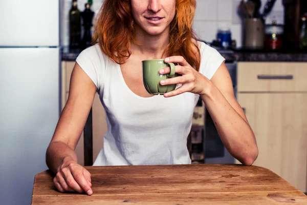 Vrouw drinken uit een beker in haar keuken — Stockfoto