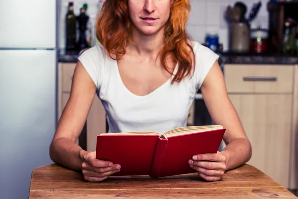 Woman reading a book in her kitchen — Stock Photo, Image