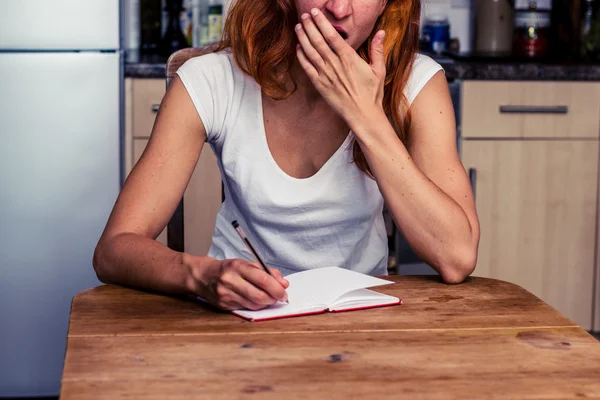 Mulher cansada escrevendo em sua cozinha — Fotografia de Stock