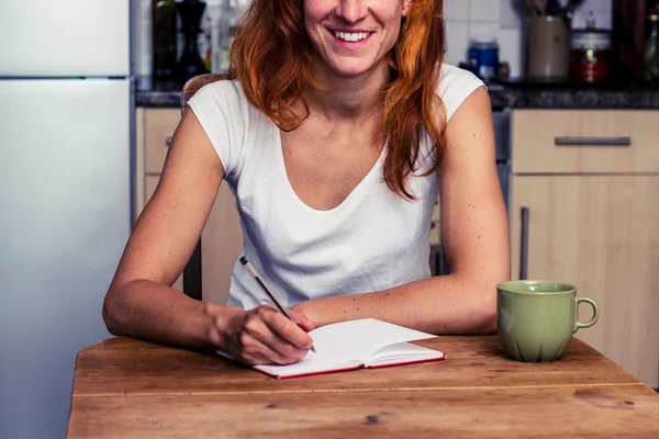 Щаслива жінка пише на своїй кухні — стокове фото