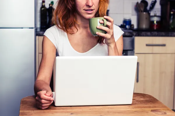 Kvinna dricker kaffe och arbetar på bärbar dator — Stockfoto