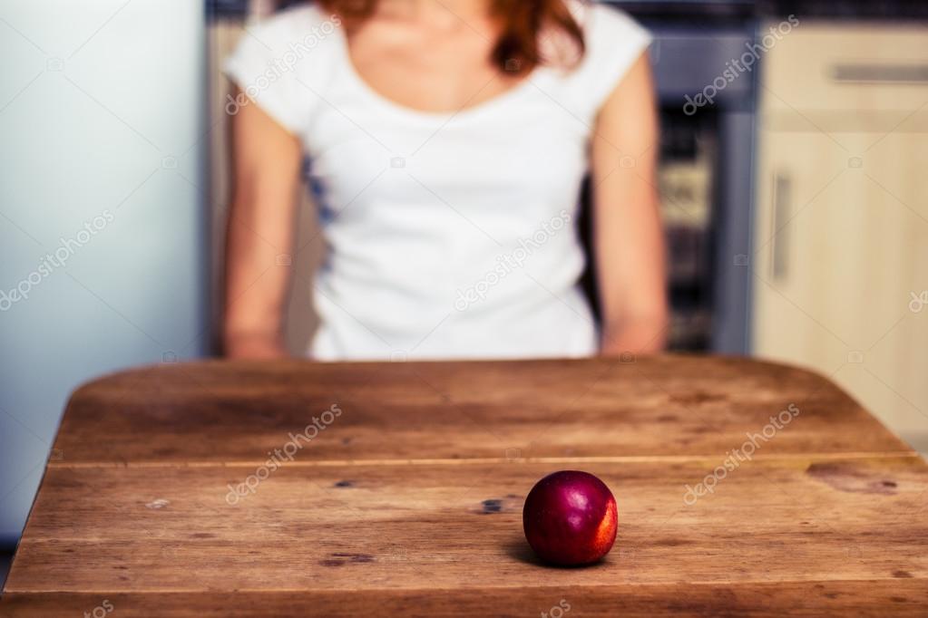 Woman with a peach in front of her in kitchen