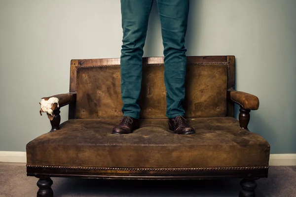 Человек в обуви, стоящий на диване — стоковое фото