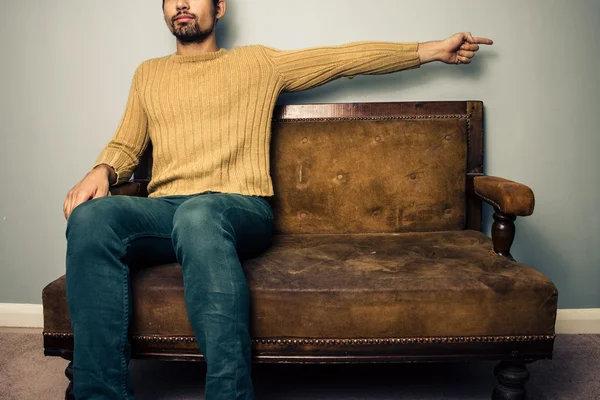 Fiatal férfi a kanapén mutat jobb — Stock Fotó