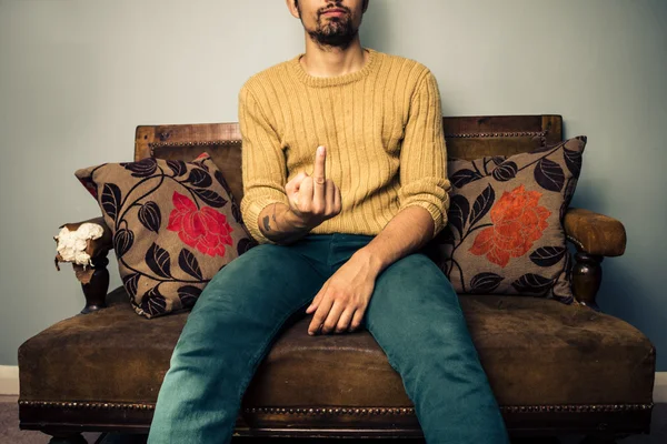 Mladý muž na pohovce zobrazování obscénní gesto — Stock fotografie