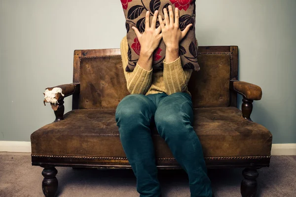 Nervous young man on couch hiding behind cushion — Stock Photo, Image