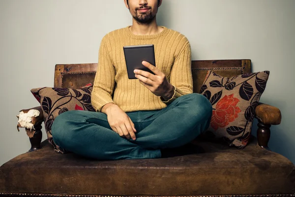 Junger Mann sitzt auf Sofa und liest auf Tablet — Stockfoto