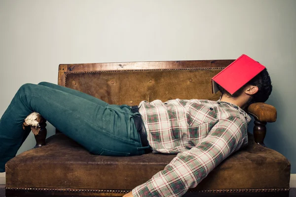 Hombre durmiendo en un viejo sofá con libro cubriéndose la cara — Foto de Stock