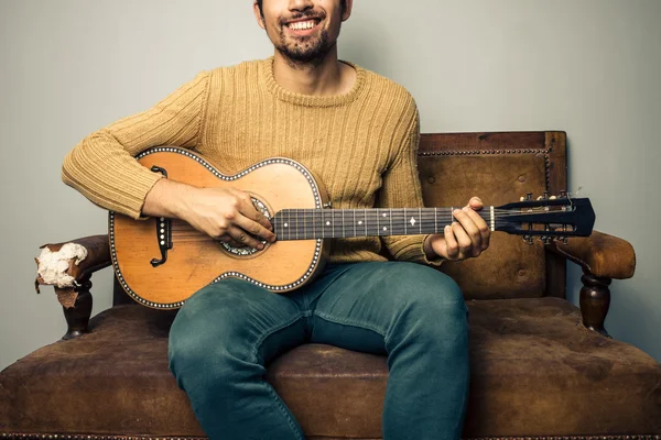 Szczęśliwy młody mężczyzna gra na gitarze na starej kanapie — Zdjęcie stockowe