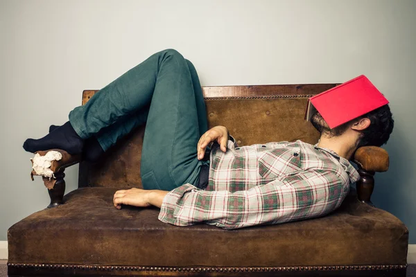 Hombre durmiendo en un viejo sofá con libro cubriéndose la cara —  Fotos de Stock
