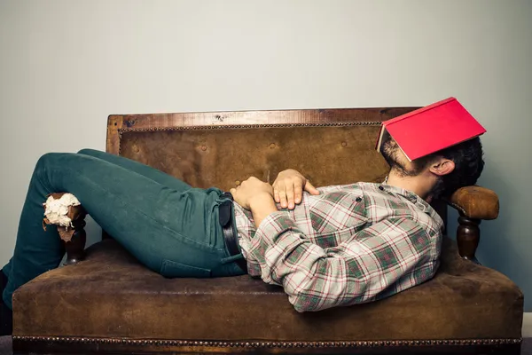 Hombre durmiendo en un viejo sofá con libro cubriéndose la cara — Foto de Stock