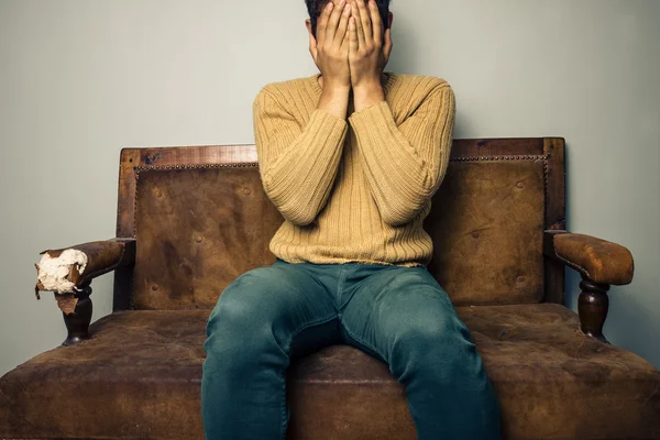 Rozrušený mladý muž seděl na staré pohovce — Stock fotografie
