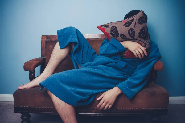 Man in dressing gown sleeping with face behind cushion — Stock Photo, Image