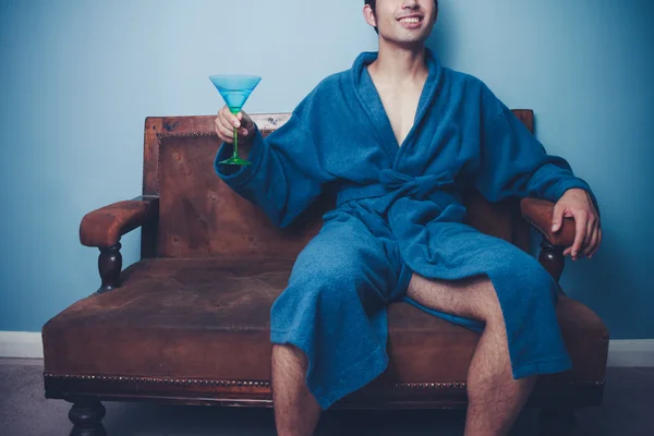 Happy young man in dressing gown drinking martini — Stock Photo, Image