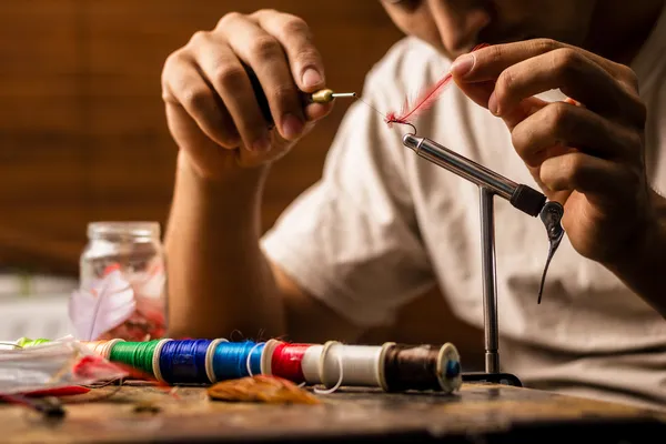 Close up on young man's hands tying a fly for fishing — Stock Photo, Image