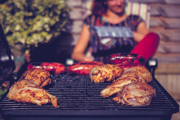 Kip en worsten op de barbecue met vrouw in achtergrond — Stockfoto
